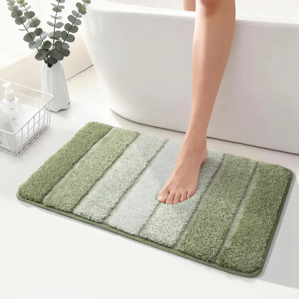 Green striped bath mat on a bathroom floor with a foot stepping onto it.