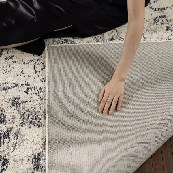 Close-up of a textured rug corner with a neutral color palette on a wooden floor.