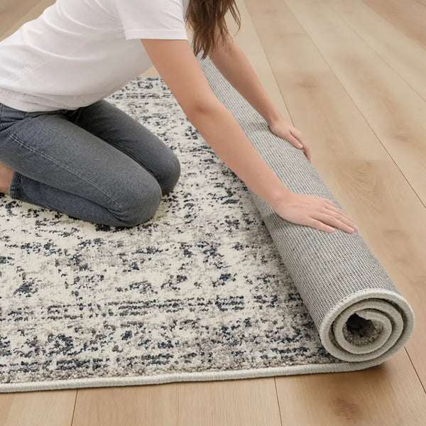 Person unrolling a patterned rug on a wooden floor