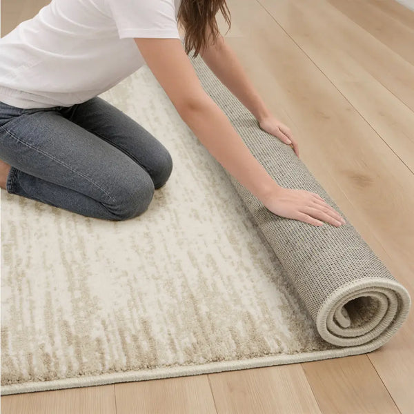 Person rolling out a beige rug on a wooden floor