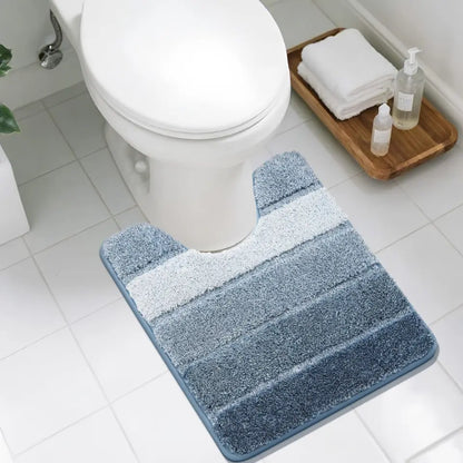 Blue striped U shaped bath mat in front of a toilet with a wooden tray holding towels and bottles.