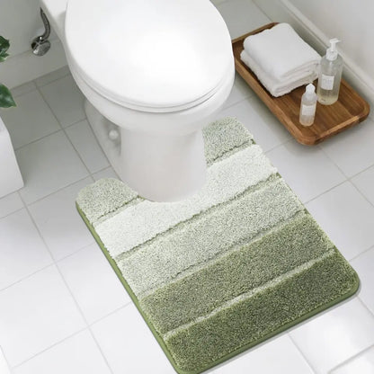 Green U shaped bath mat on a bathroom floor with a toilet and wooden tray in the background.