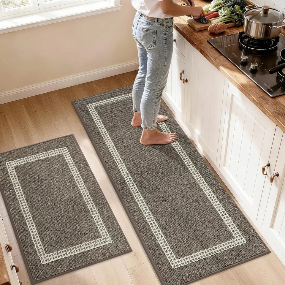 Person standing on a long brown rug with a white border in a kitchen.
