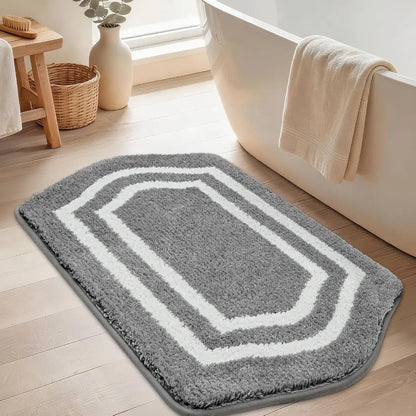 Grey bath mat with white border on a wooden floor next to a bathtub.