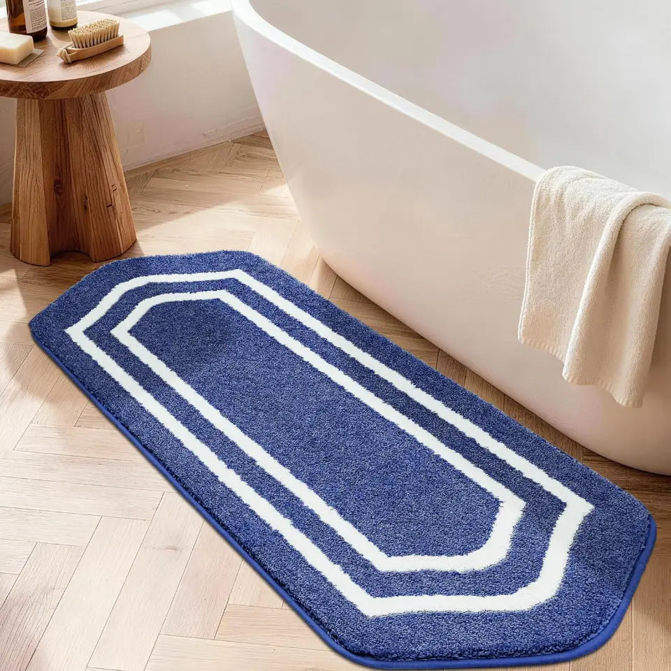 Blue bath mat with white border on a wooden floor next to a bathtub.