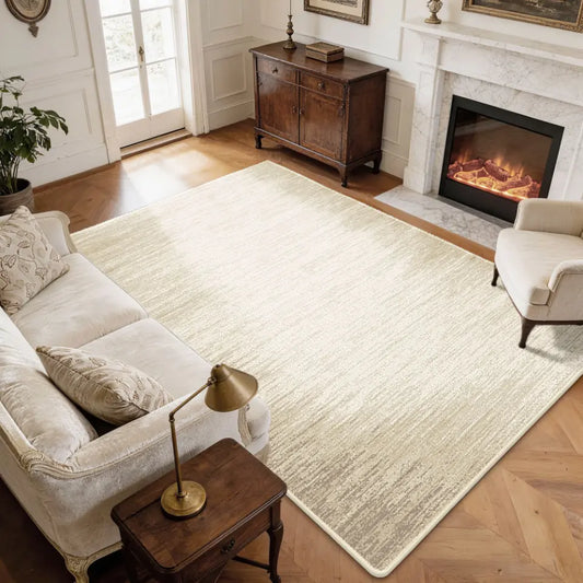 Living room with a large taupe & cream rug, sofa, armchair, and fireplace.