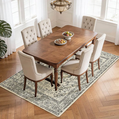 Dining room with wooden table and upholstered chairs on a faded grey & cream patterned rug.