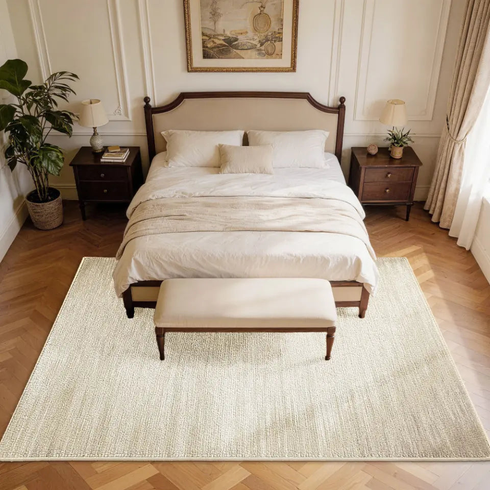 Neatly made bed in a bedroom with a taupe & cream rug, bench, and decor.