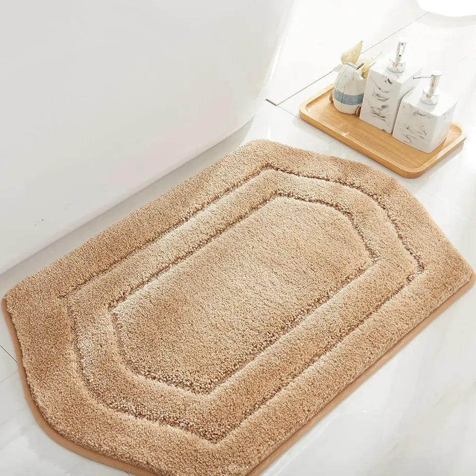 Beige bath mat on a bathroom floor with a wooden tray and toiletries in the background.