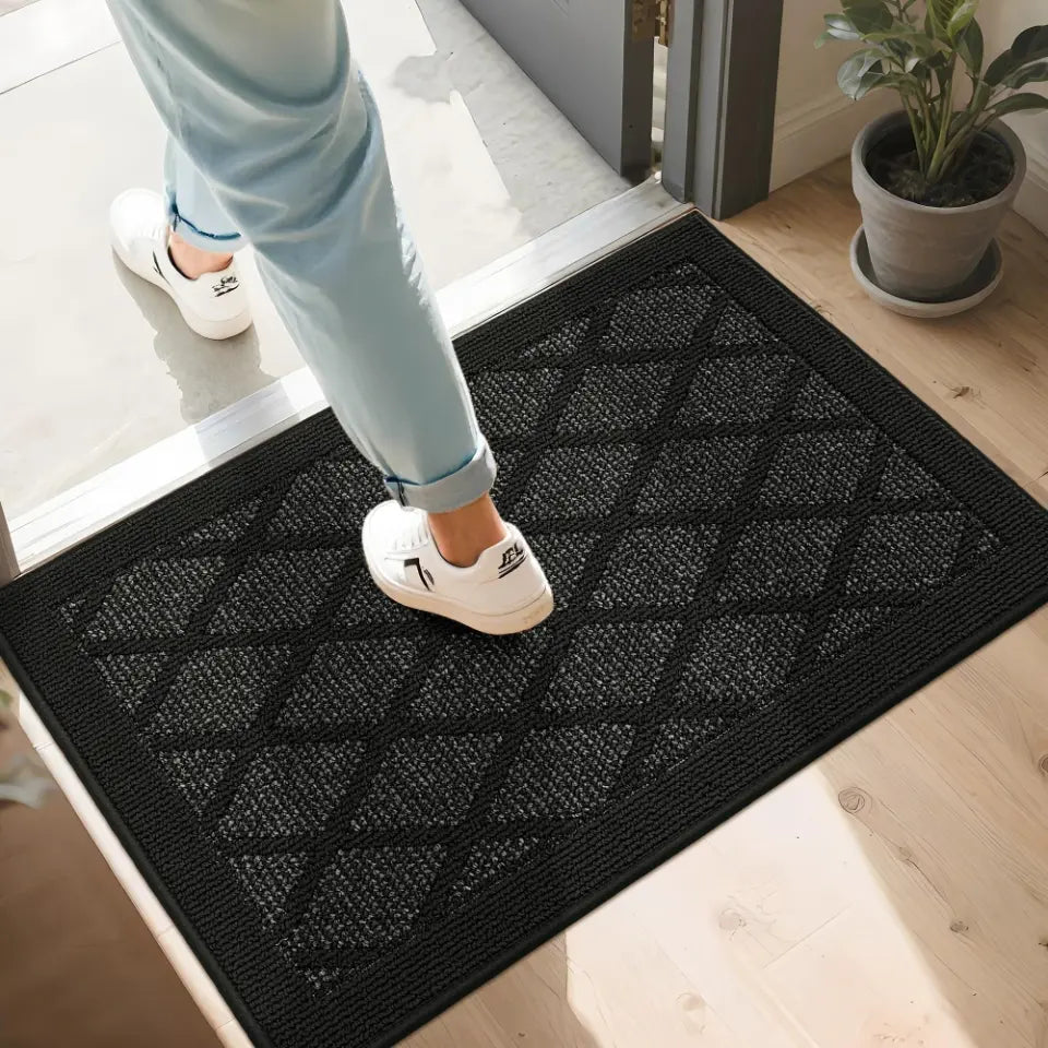 Person stepping onto a black doormat with a geometric pattern, wearing white shoes.