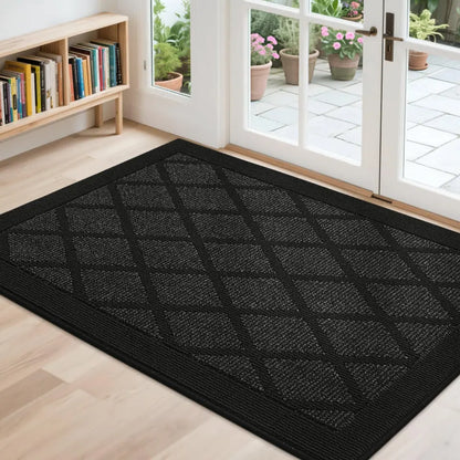 Black doormat with diamond pattern on a wooden floor, leading to a glass door with outdoor view.