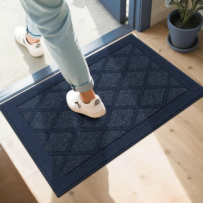 Person stepping onto a navy doormat with a geometric pattern, wearing white shoes.
