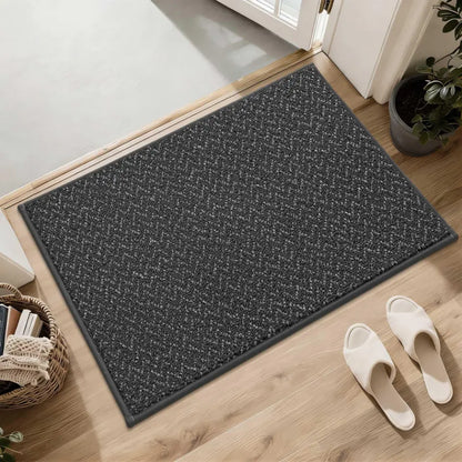 Dark gray doormat on a wooden floor with white slippers and a plant in the background.