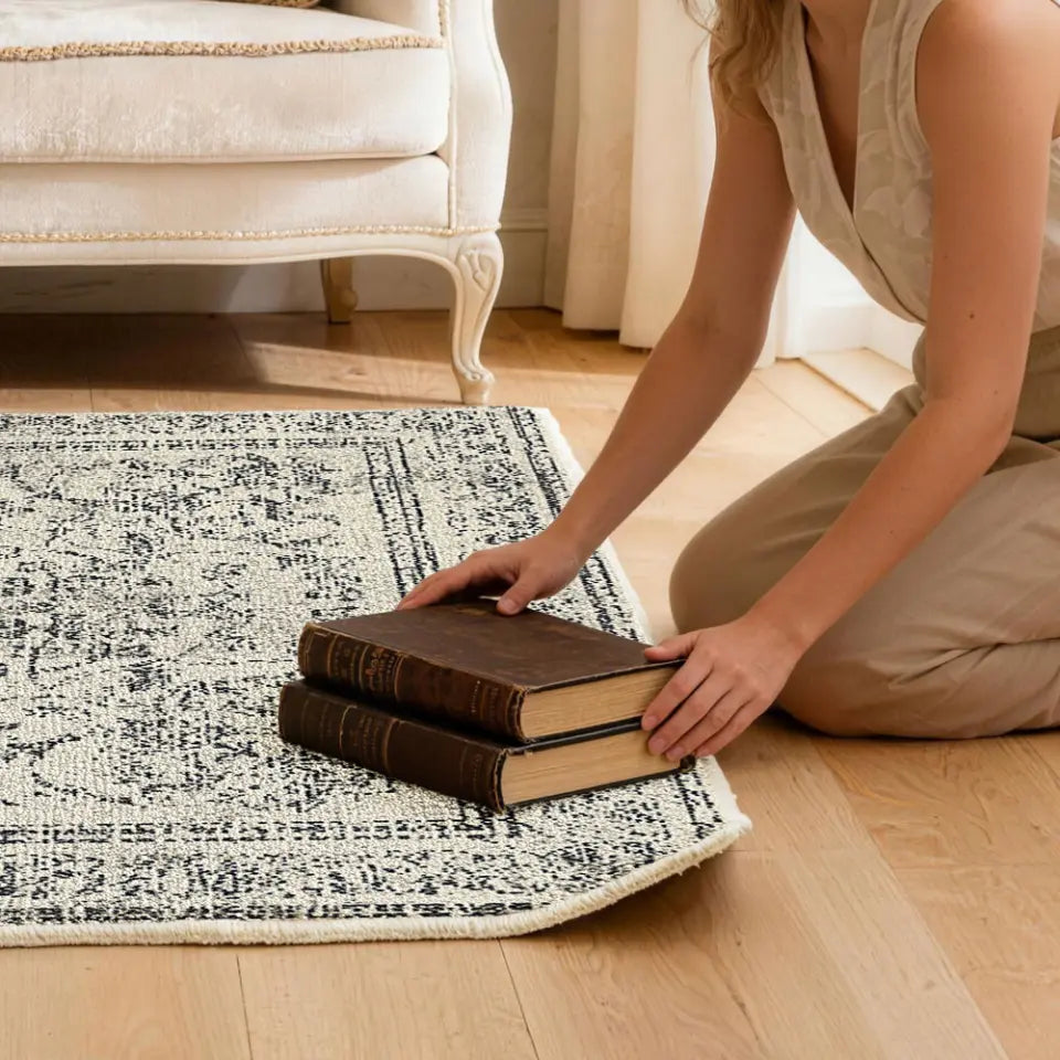 Person arranging books on a patterned rug to flatten the corner of rug