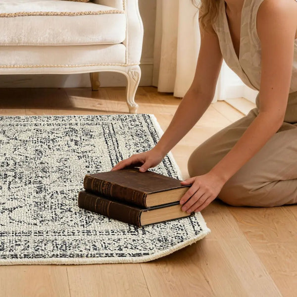 Person arranging books on a patterned rug to flatten the corner of rug