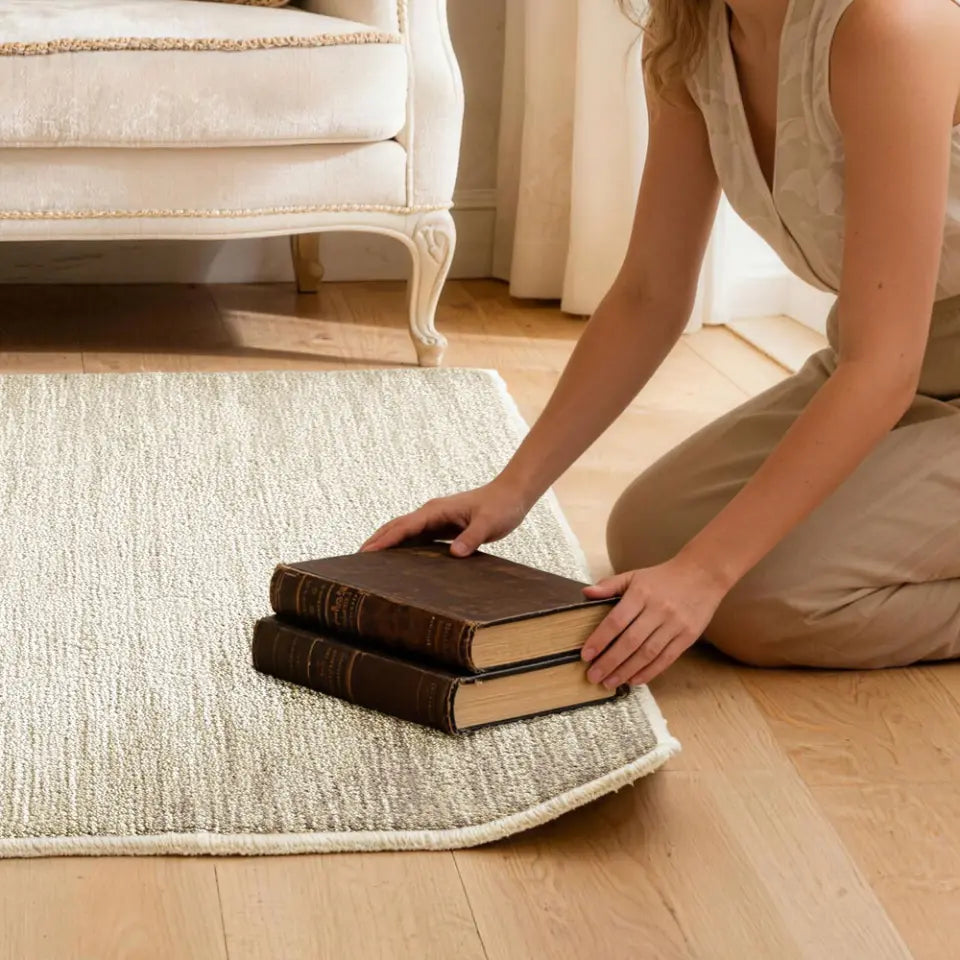 Person arranging books on a patterned rug to flatten the corner of rug