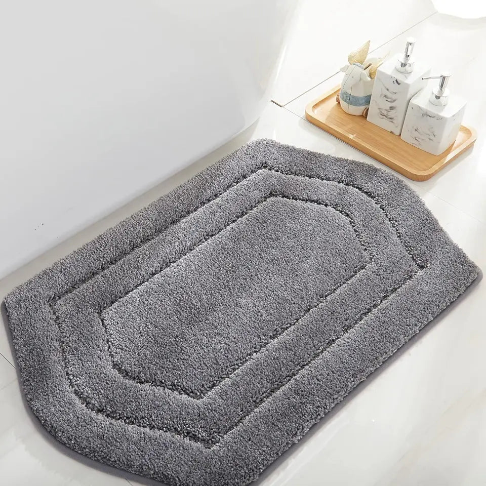 Grey bath mat on a bathroom floor with a wooden tray and toiletries in the background.