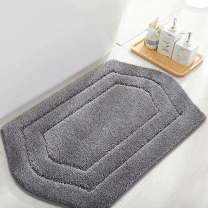 Grey bath mat on a bathroom floor with a wooden tray and toiletries in the background.