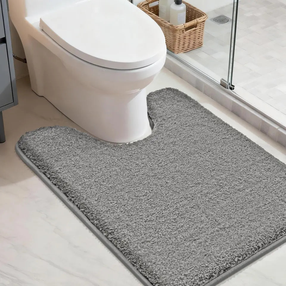 Grey u shaped toilet rug in front of a toilet in a bathroom setting