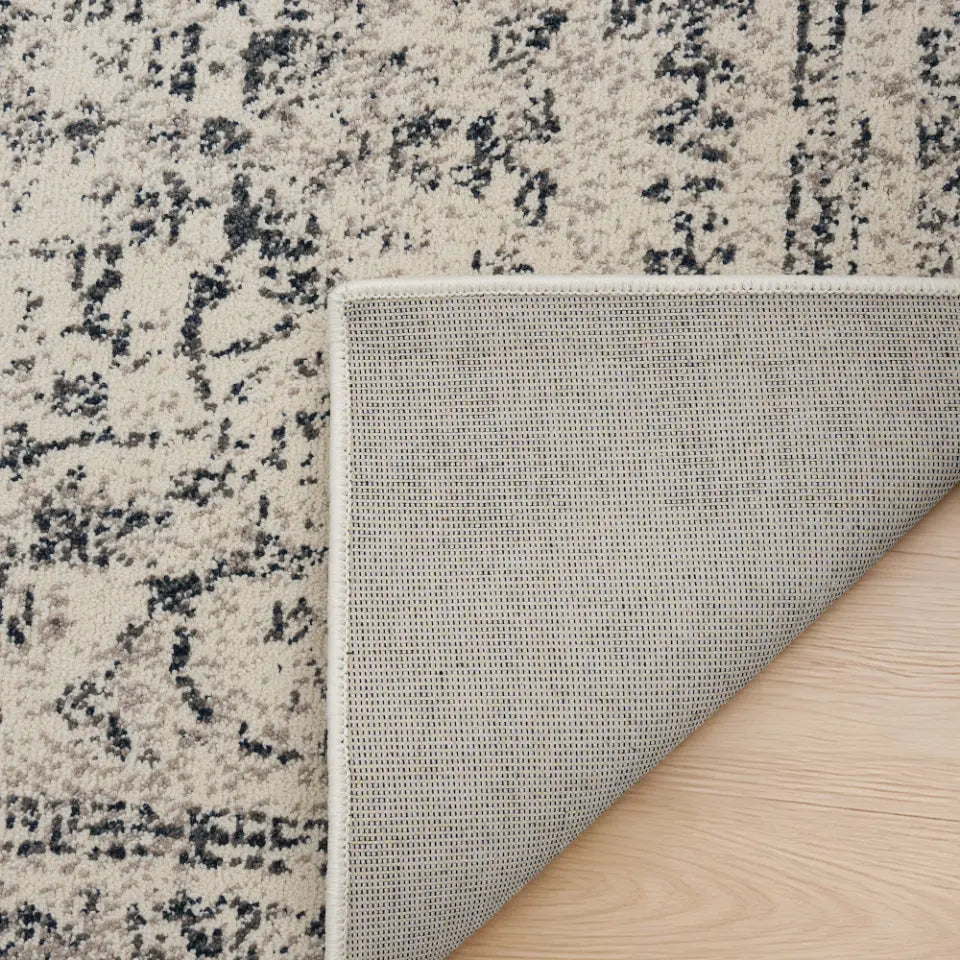 Close-up of a textured rug corner with a neutral color palette on a wooden floor.