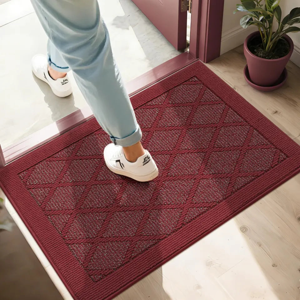 Person stepping onto a red doormat with a patterned design.