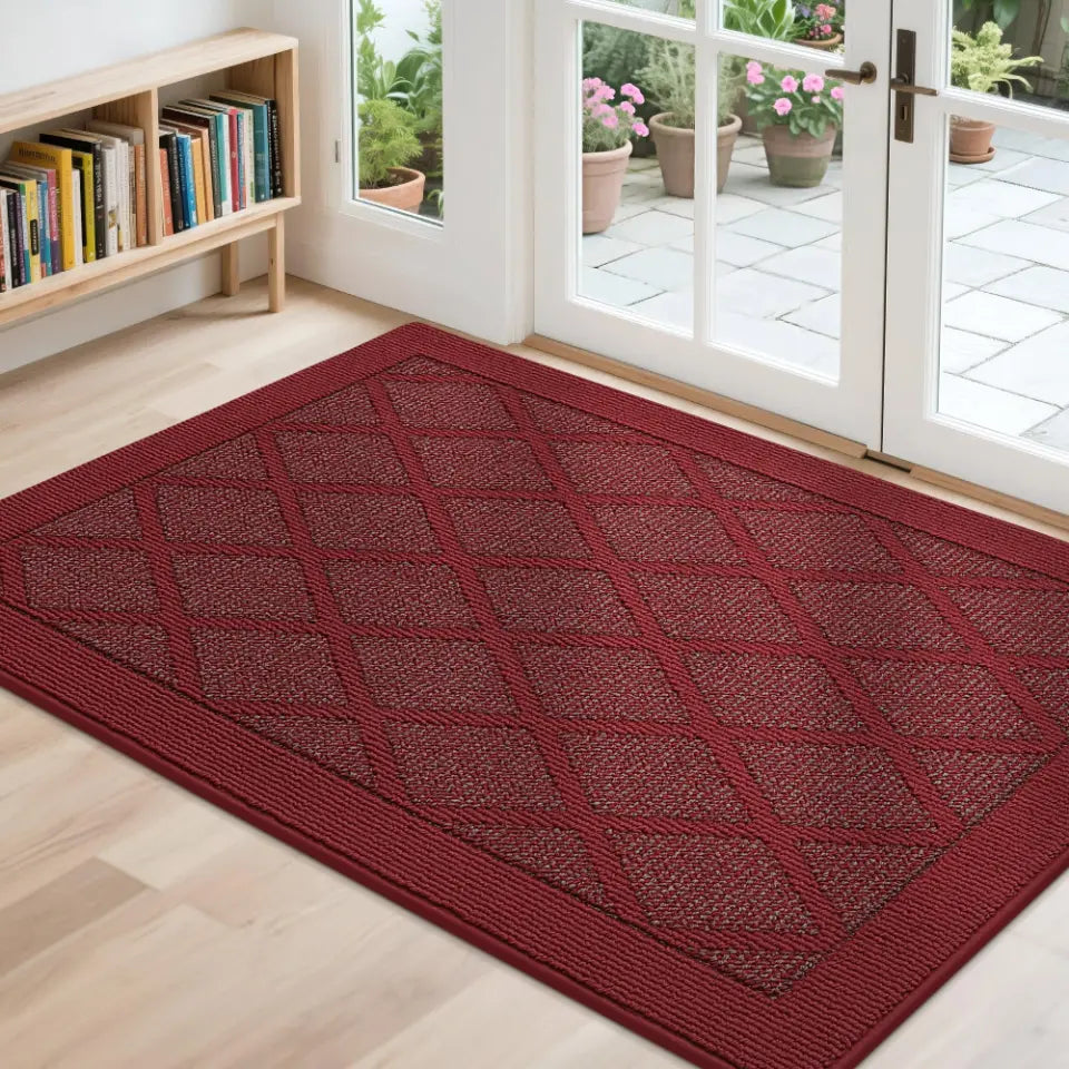 Red doormat with diamond pattern on a wooden floor, leading to a glass door with outdoor view.