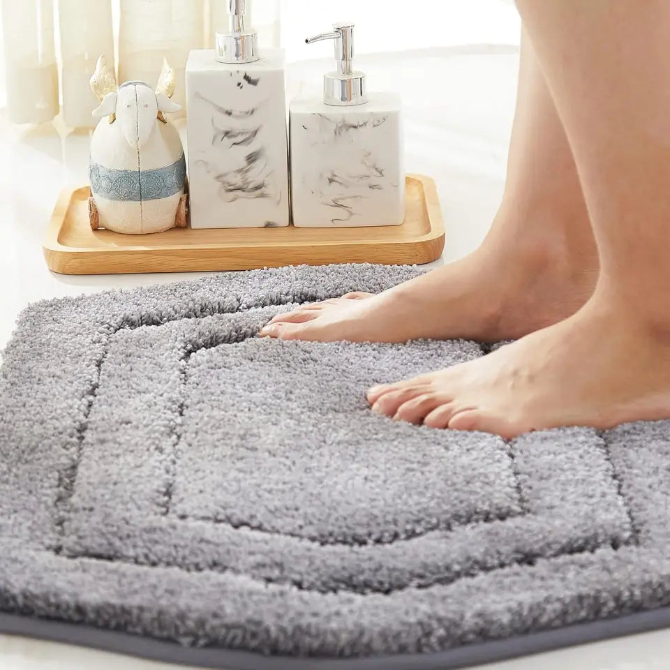 Grey bath mat with feet stepping onto it, bathroom setting with toiletries in the background.
