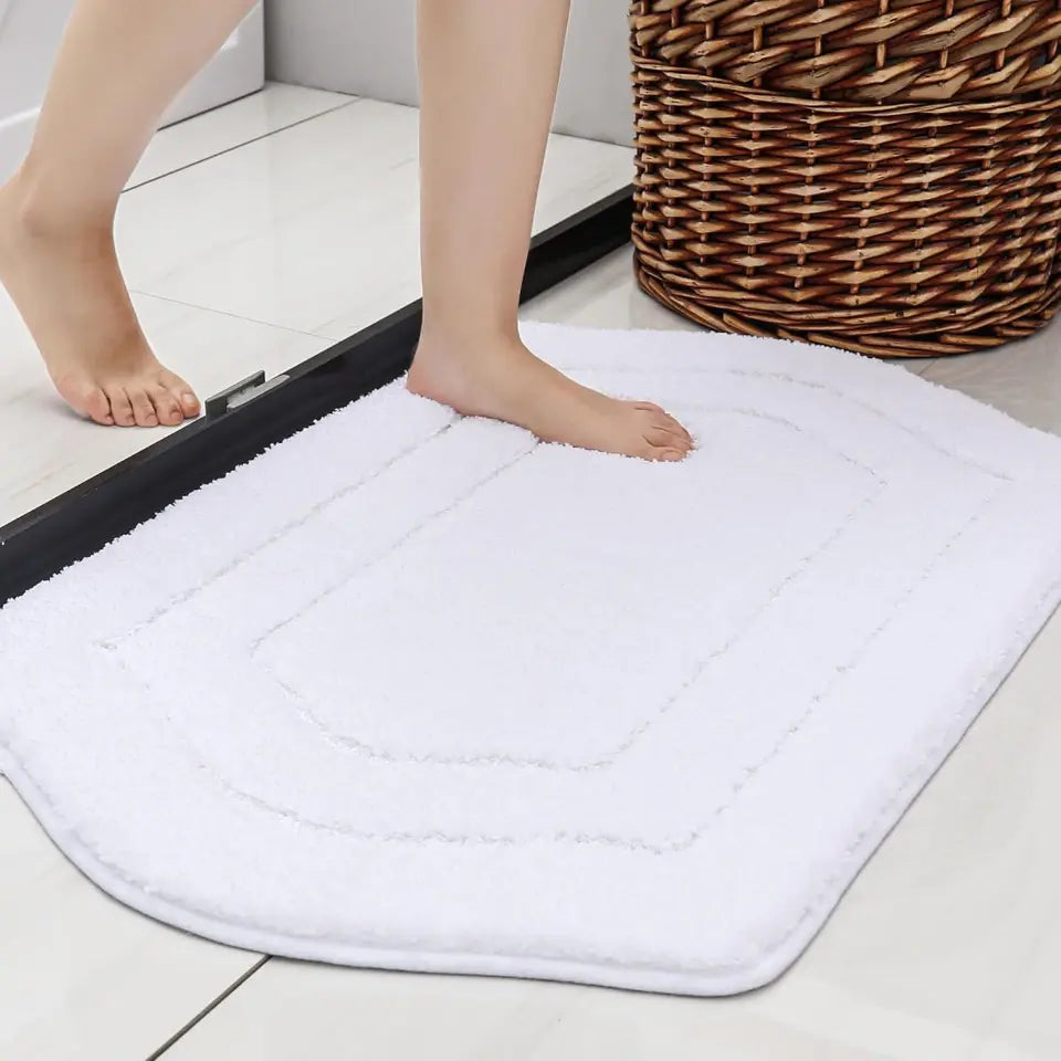 White bath mat on a bathroom floor with a wicker basket in the background.