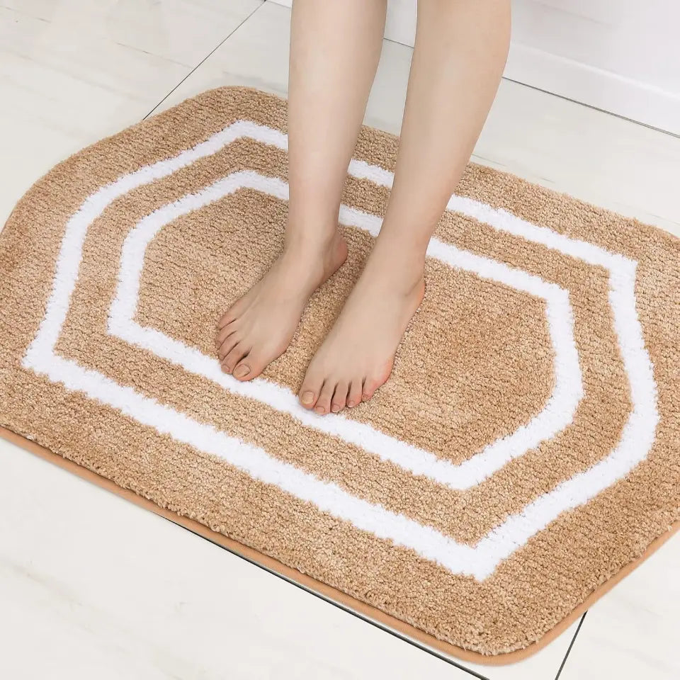 Person standing on a beige bath mat with white geometric patterns on a light wooden floor.